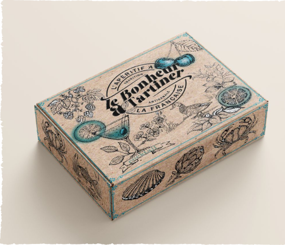 Une boîte en carton kraft de la marque "La Cerise Sur l'Apéro", illustrée de dessins vintages en noir et bleu turquoise représentant des ingrédients d'apéritif (cerises, cocktail, crabe, coquillages).